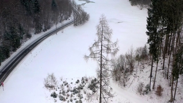 无人机向上飞行，在恶劣的冬季天气下，可以看到一条空无一人、蜿蜒曲折的高山公路，以及一条河流和森林被白雪覆盖的山谷视频素材