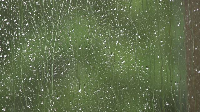 雨滴顺着窗户表面流下。外面夏天下着大雨。大风和雨点落在阳台的玻璃窗上。外面戏剧性的雷雨视频素材