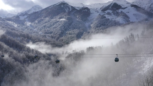 滑雪索道移动之间的雪山在雾霾鸟瞰图。滑雪电梯将人们运送到多云的山背景雪坡。冬季度假村从无人机上方视频素材