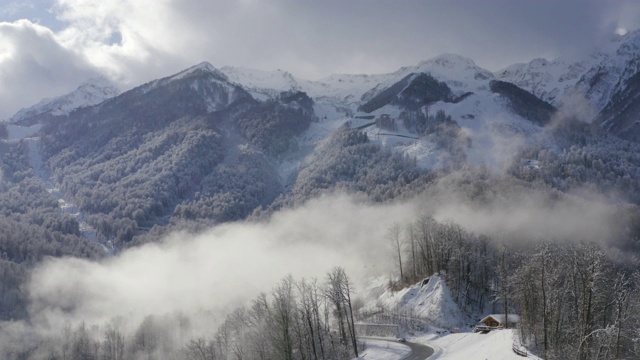 美丽的山峰在云雾中从无人机飞行。冬季高山和森林在雾霾空中景观。从上面看，是冬季度假胜地的高地和丘陵。无人机降落在蜿蜒的道路上视频素材