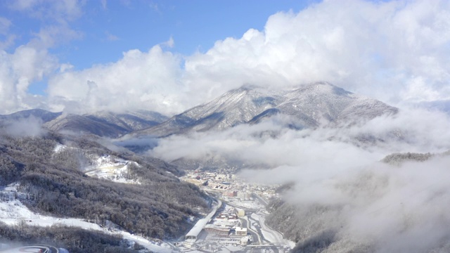 冬季城市景观之间的雪山覆盖林地。鸟瞰图雪城在冬季山谷。无人机在山谷的冬季高地上观看蓝天和云彩视频素材