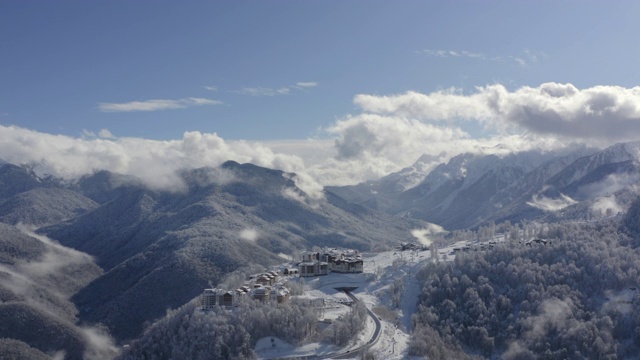 雪峰上的山村在云雾缭绕的天空上降落无人机。鸟瞰图雪山度假区蜿蜒道路。令人叹为观止的雪山和林地在雾天。第1部分视频素材