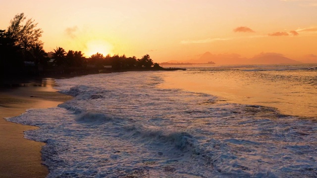 美丽的海滩在橙色夕阳下与剪影的背景。在法国波利尼西亚的帕皮提，强烈的海浪在沙滩上破碎，鸟瞰图视频素材