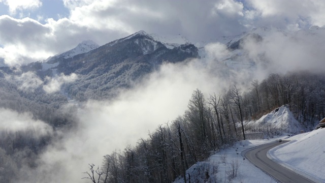 美丽的山峰在云雾中从无人机起飞。冬季高山和森林在雾霾空中景观。从上面看，是冬季度假胜地的高地和丘陵。无人机降落在蜿蜒的道路上视频素材