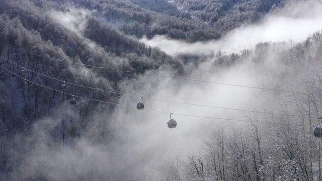 滑雪电梯移动在白色雪山云森林在低地。无人机视野滑雪升降机运送滑雪者和滑雪板滑雪者雪坡上的山区度假村在冬季自然景观视频素材