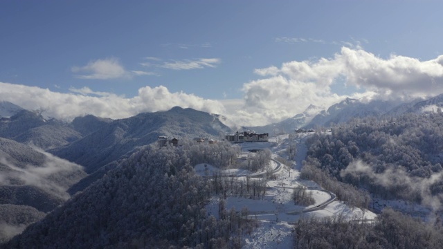 雪峰上的山村在云雾缭绕的天空上降落无人机。鸟瞰图雪山度假区蜿蜒道路。令人叹为观止的雪山和林地在雾天。第二部分视频素材