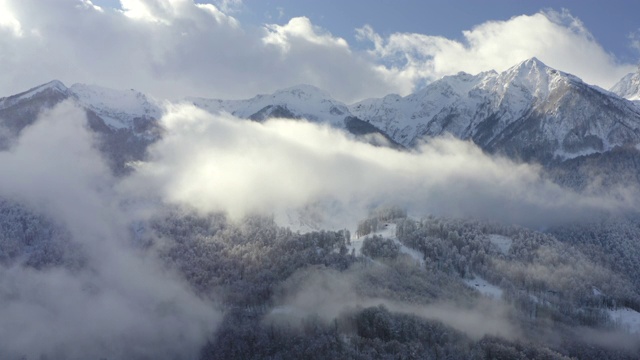 令人惊叹的冬季景观从无人机雪峰多云的天空背景。无人机空中拍摄冬天山上覆盖的积雪和森林。白色的薄雾笼罩着山谷和林地视频素材