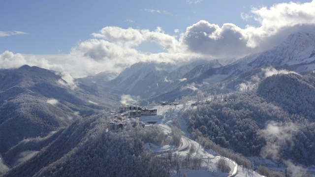 山村雪峰上云雾缭绕的天空从无人机上掠过。鸟瞰图雪山度假区蜿蜒道路。令人窒息的景色雪山和林地在雾天空的背景视频素材