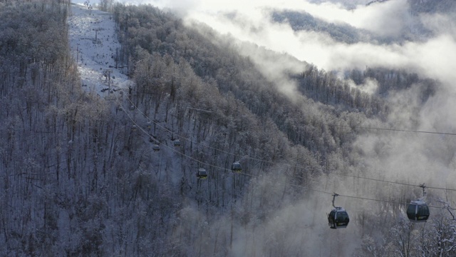 滑雪索道在雪山之间在薄雾中跟随鸟瞰图。滑雪电梯将人们运送到多云的山背景雪坡。冬季度假村从无人机上方视频素材