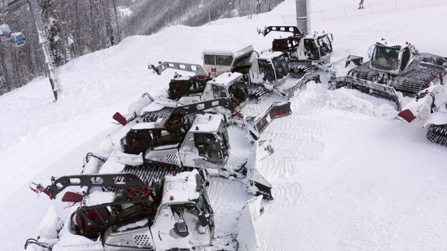 红色雪车站在雪山滑雪场的雪地停车场上。山顶滑雪场冬季斜坡上无人机雪美容机的空中降落视图视频素材