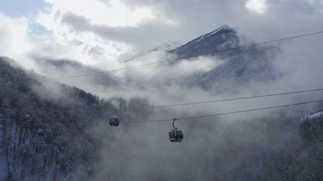 无人机观看滑雪缆车移动在雾蒙蒙的林地在冬季度假村。空中景观滑雪电梯运送运动员在滑雪场雪坡之间。雪山滑雪场在多云的大山里视频素材