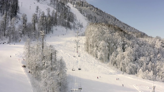 无人机飞过滑雪场雪坡上移动的滑雪电梯。顶部鸟瞰图滑雪缆车运送滑雪者和滑雪板在雪山。冬季景观滑雪场在多雪的高地视频素材