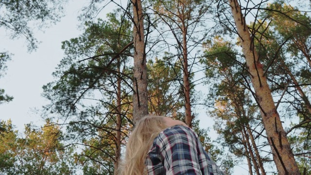 年轻的女孩在松树林中望着天空。浪漫的女孩转过身，抬头看着树林里高高的松树。视频素材