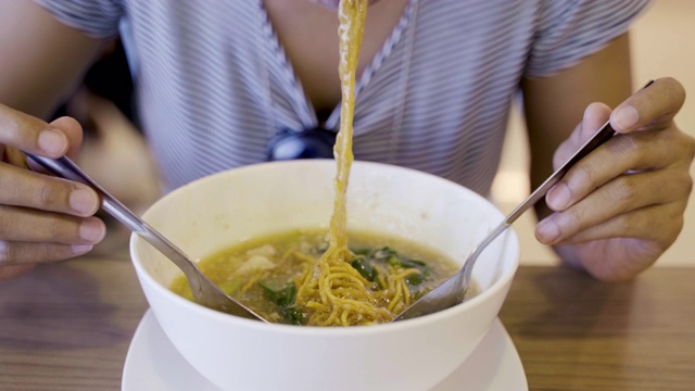 年轻的亚洲女人饿着吃炒面猪肉和甘蓝浸在肉汁(Radna)著名的泰国食物，吃看起来很好吃。视频素材