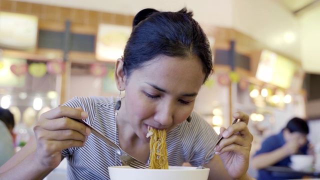 年轻的亚洲女人饿着吃炒面猪肉和甘蓝浸在肉汁(Radna)著名的泰国食物，吃看起来很好吃。视频素材