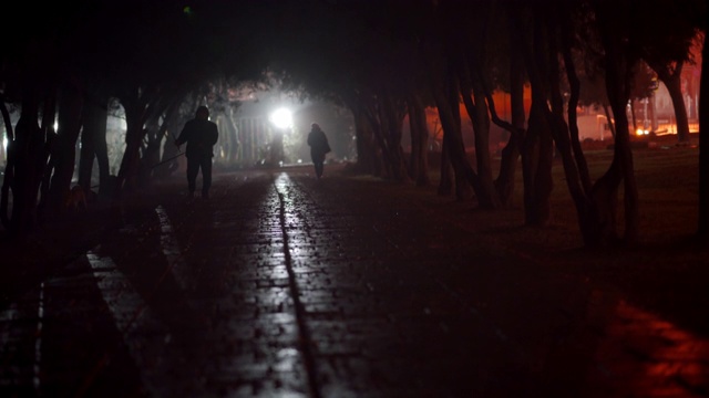 夜晚的城市景象，人们的剪影在黑暗的人行道上行走。视频素材