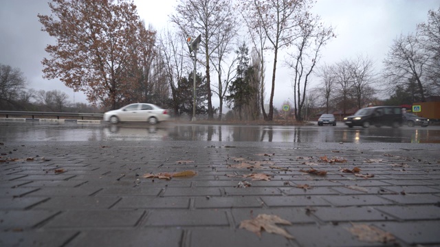 秋天的雨天，城市交通在潮湿的道路上行驶，汽车驶过一个车轮溅起水花的水坑。视频素材