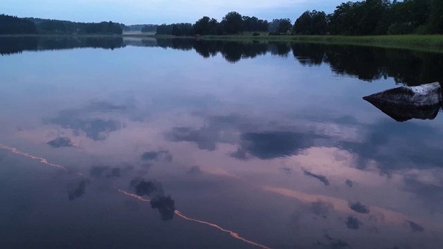 美丽的日落在平静的夏夜。湖岸与绿色的树木和植物反射在水晶干净镜面水面。天空乌云密布。视频素材