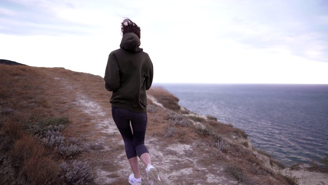 在海边进行跑步训练。美丽的女人在户外晨跑，穿着运动衫和打底裤视频素材