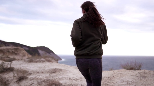 女跑步运动员正在海边的一个高悬崖上训练。在海边的大自然中晨跑。有氧运动在运动衫跟踪镜头视频素材