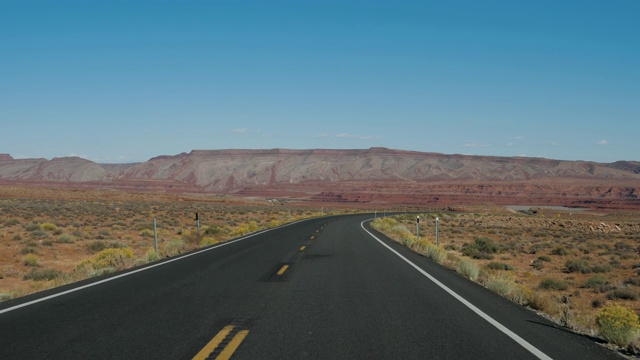 在高速公路上驾驶穿越沙漠在红色岩石的背景视频素材