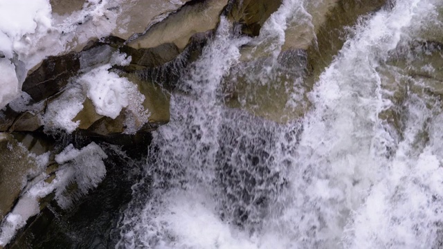 在冬天从山溪和石滩中急速流动的水和雪。瀑布。慢动作视频素材