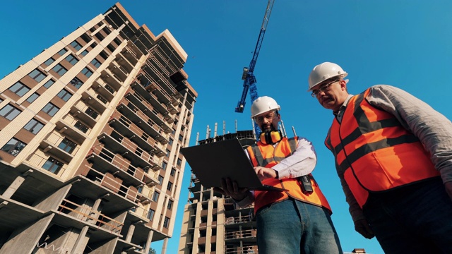 在建筑工地工作的建筑承包商。男人们站在一个网站上，用一台笔记本电脑工作。视频素材