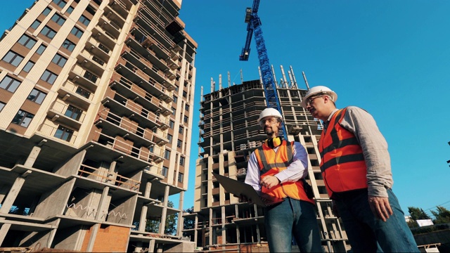 两名工人站在建筑物附近检查。在建筑工地工作的建筑承包商。视频素材