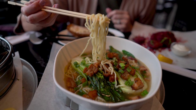 在餐馆里，人们从拉面碗里舀出面条，里面有脆皮五花肉和蔬菜视频下载