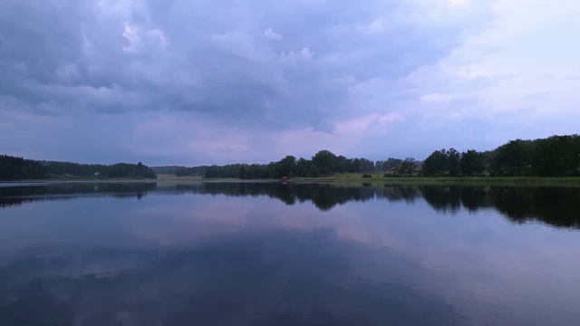 美丽的日落在平静的夏夜。湖岸与绿色的树木和植物反射在水晶干净镜面水面。天空乌云密布。视频素材