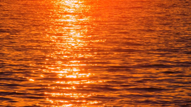 美丽的海景，夕阳在海水中倒映。路人拿着笔记本走过。热岩浆调色板。日落时不寻常的海景。海水反映了日落。海水中反射的阳光视频素材