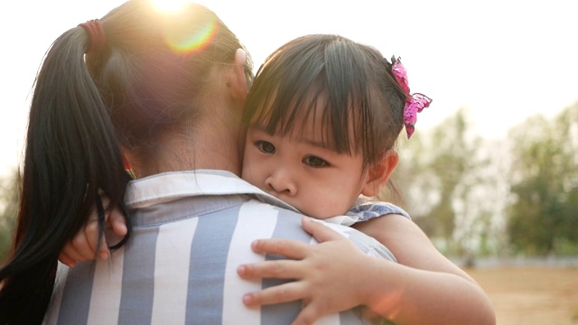 亚洲母亲安慰她的女儿拥抱在夏季公园。一个小孩在田野里摔倒了，哭了起来。家庭中的爱的概念。视频素材