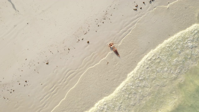 海浪拍打着躺在海滩上的比基尼女子视频素材