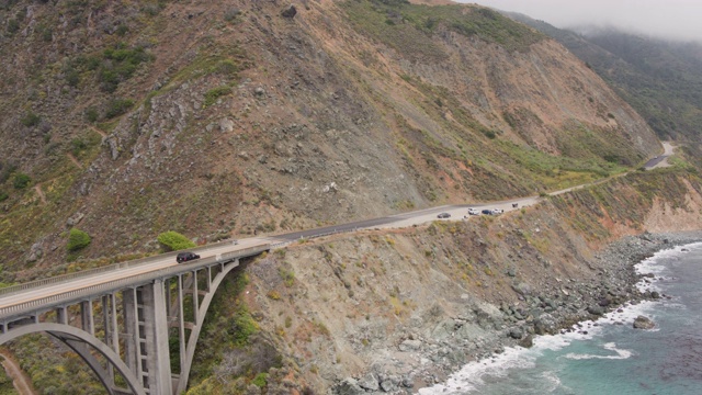 无人机拍摄的一座桥，俯瞰岩石、陡峭的海岸线公路(大苏尔，太平洋海岸公路，加利福尼亚)视频素材