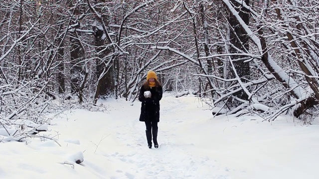 一个快乐的女孩走过冬天的森林，微笑，有一个好心情，玩雪，扔雪球视频下载