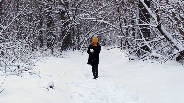 一个快乐的女孩走过冬天的森林，微笑着，有一个好心情，玩雪，吹雪花在雪花的背景视频下载