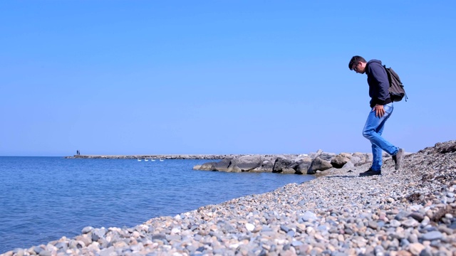 男游客在春假来到海边，坐在石滩上看海。视频素材