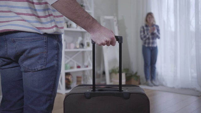 一名拿着旅行袋的陌生白人男子和在背景下哭泣的模糊女子。年轻家庭离婚的肖像。感情问题，分手，婚姻困难视频素材