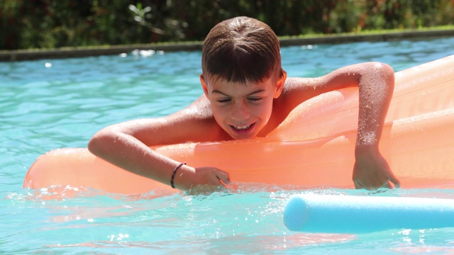 一个小男孩在游泳池里的充气床垫上玩耍视频素材