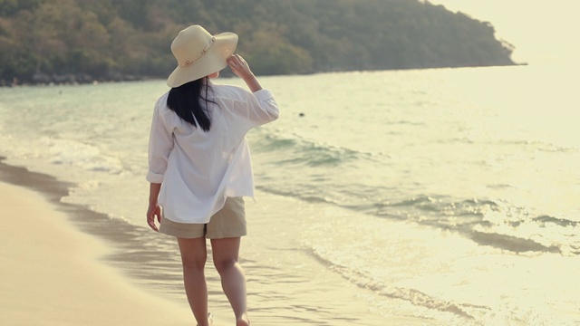 美丽的亚洲女人走在海滩上看日落快乐的乐趣旅游暑假。视频素材