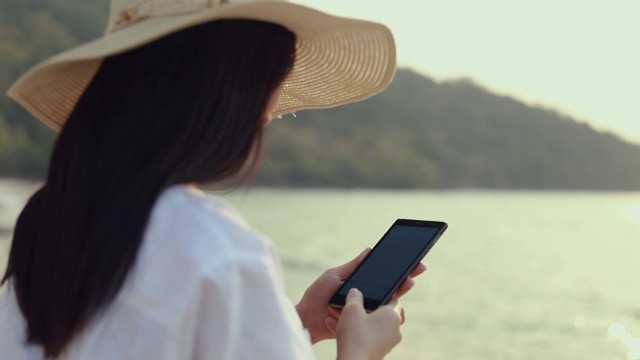 快乐的亚洲十几岁的女人拿着智能手机在海滩上拍摄美丽的日落。生活方式旅游度假夏季概念。视频素材