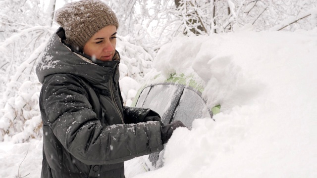 一个女人在冬天刷车里的雪的肖像。视频素材