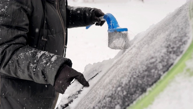 一个女人在刷汽车后窗里的雪。视频素材