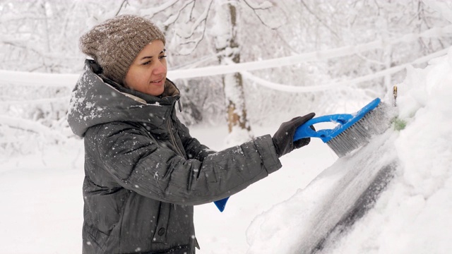 出行前用冰清洗汽车后窗的积雪。一名女子在清除车窗上的雪。视频素材