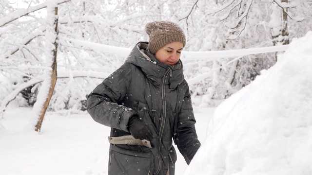 在冬天被雪覆盖的汽车里，女人打开后备箱。冬天，一位妇女在清理车上的积雪。视频素材