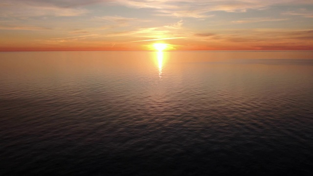 鸟瞰图飞过平静的海面朝向夕阳。美丽的金色日落在海上的全景视频素材