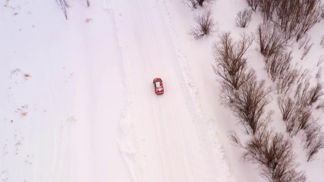 一辆橙色的汽车正在雪地上行驶。无人机鸟瞰图视频素材