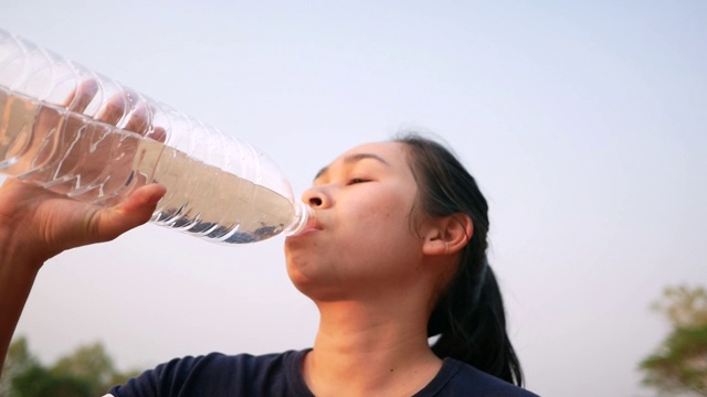 亚洲年轻女子在公园慢跑后喝塑料瓶里的水。减肥。健康的生活方式的概念。视频素材