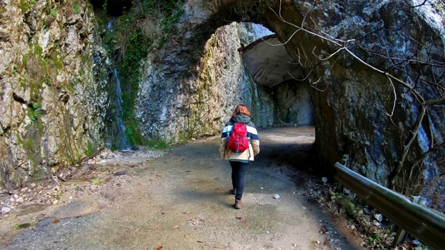 一位年轻的女摄影师背着背包走在岩石峡谷中一条美丽的山路上。山上美丽的隧道和洞穴。在山川上徒步旅行。视频素材