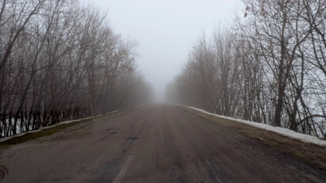 冬天的风景。透过挡风玻璃，一辆汽车在乡村道路上行驶，周围的田野和树木被浓雾覆盖。4 k视频素材